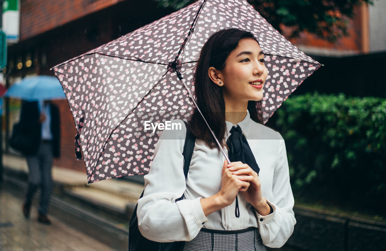 BEAUTIFUL YOUNG WOMAN LOOKING AWAY WHILE STANDING IN RAIN
