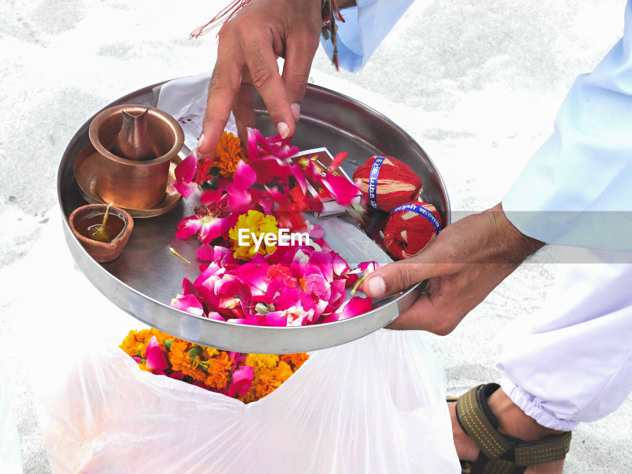 Low section of man holding plate with flowers and diya