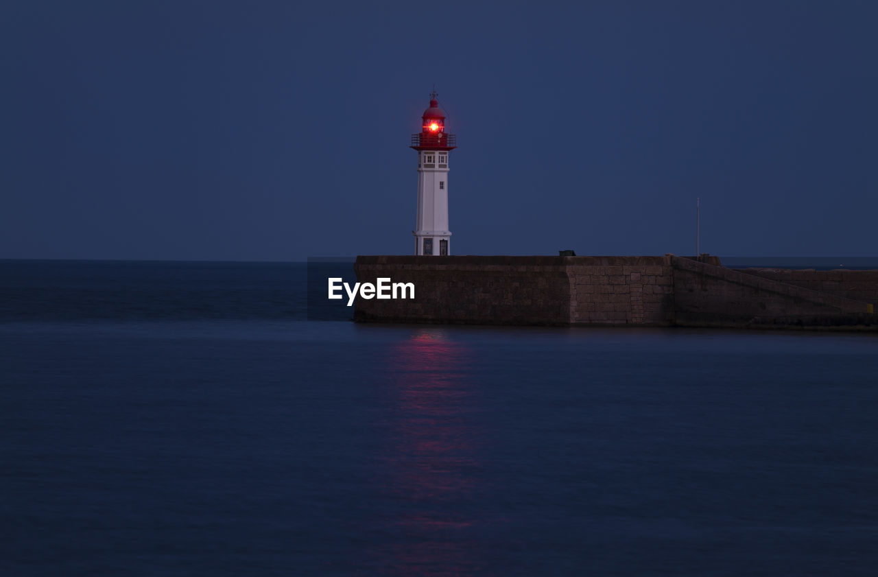 Lighthouse with red light by sea against sky at night. almeria, spain.