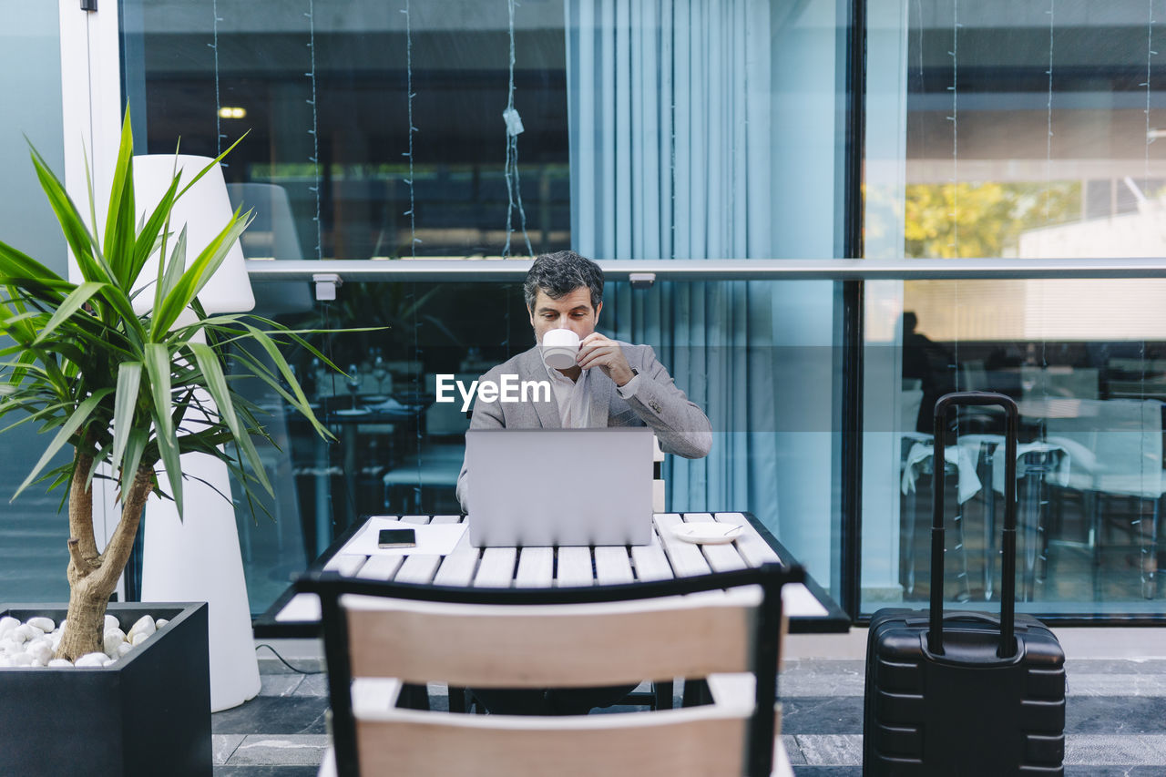 Businessman drinking coffee while sitting with laptop in cafe