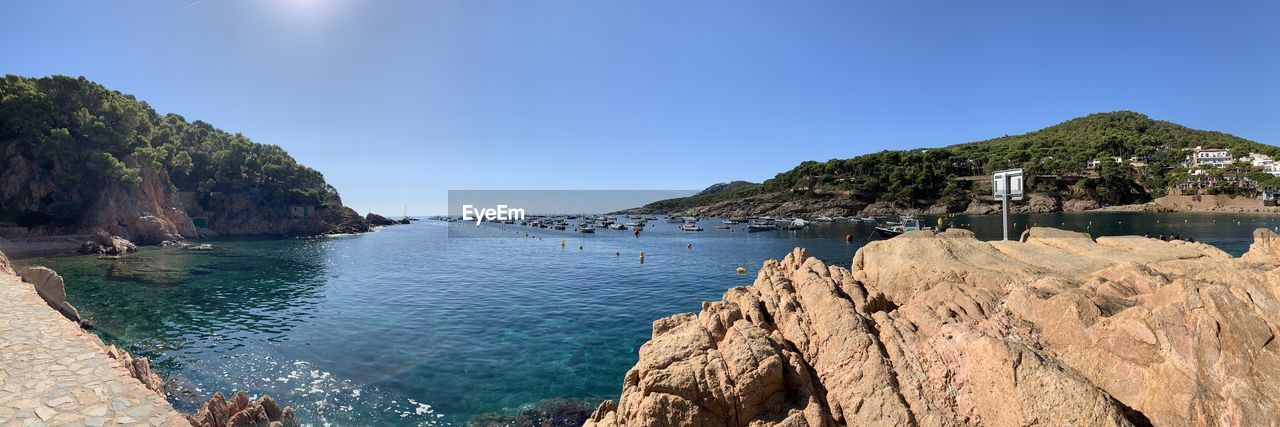 Panoramic view of sea and rocks against clear blue sky