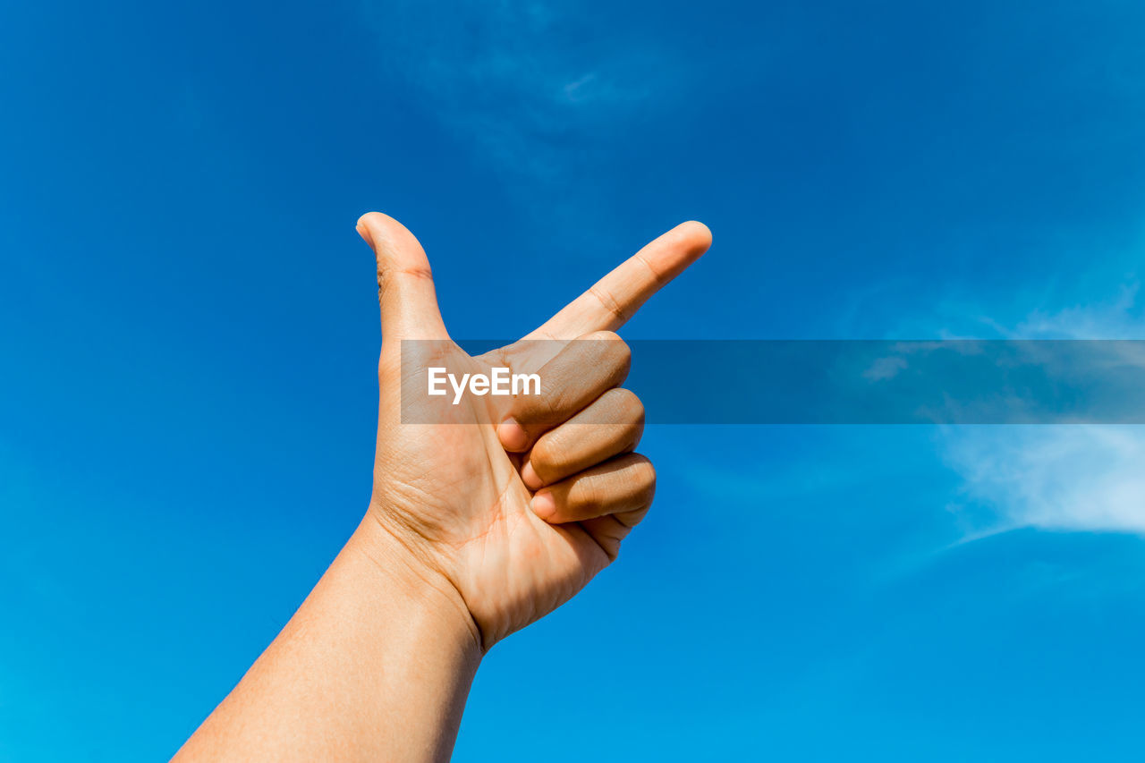 Cropped hand gesturing against blue sky