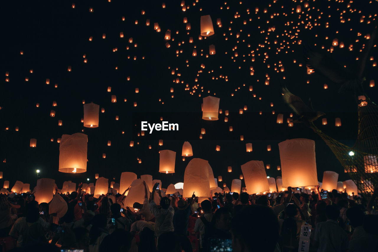 Crowd of people holding illuminated lanterns against sky at night