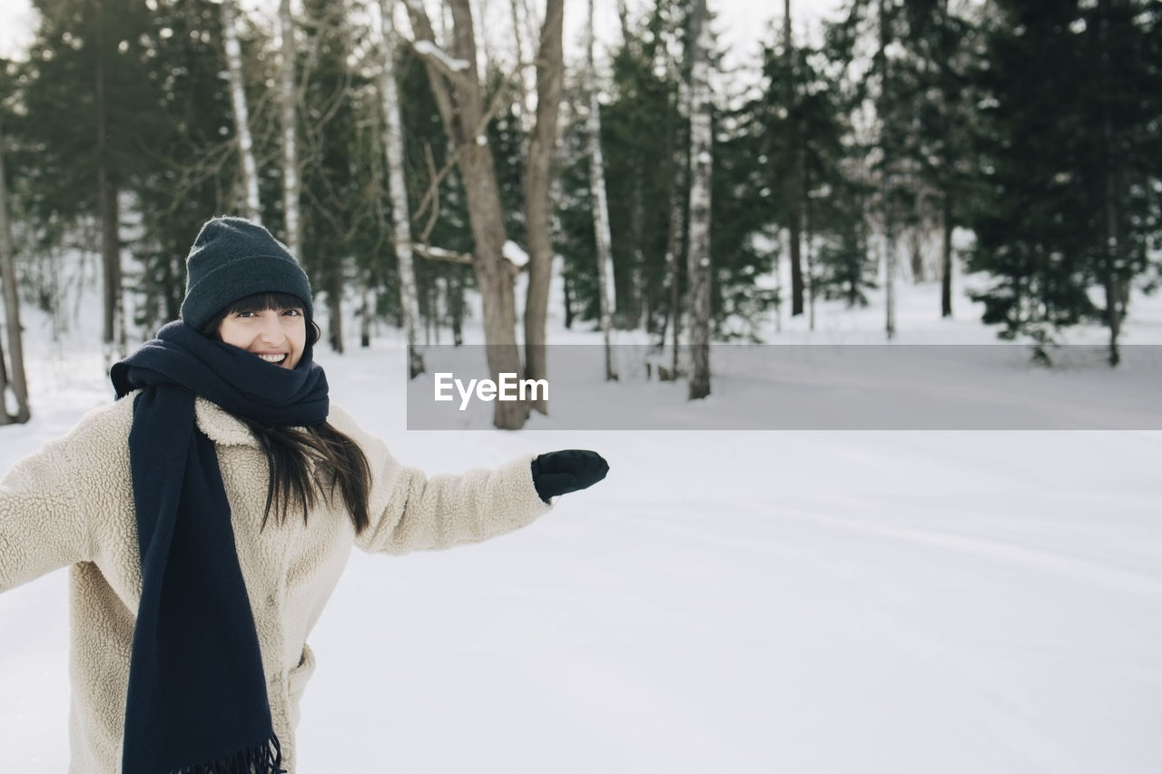 Portrait of happy woman standing with arms outstretched on snow covered landscape