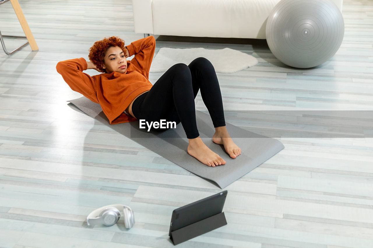 full length of young woman exercising on floor