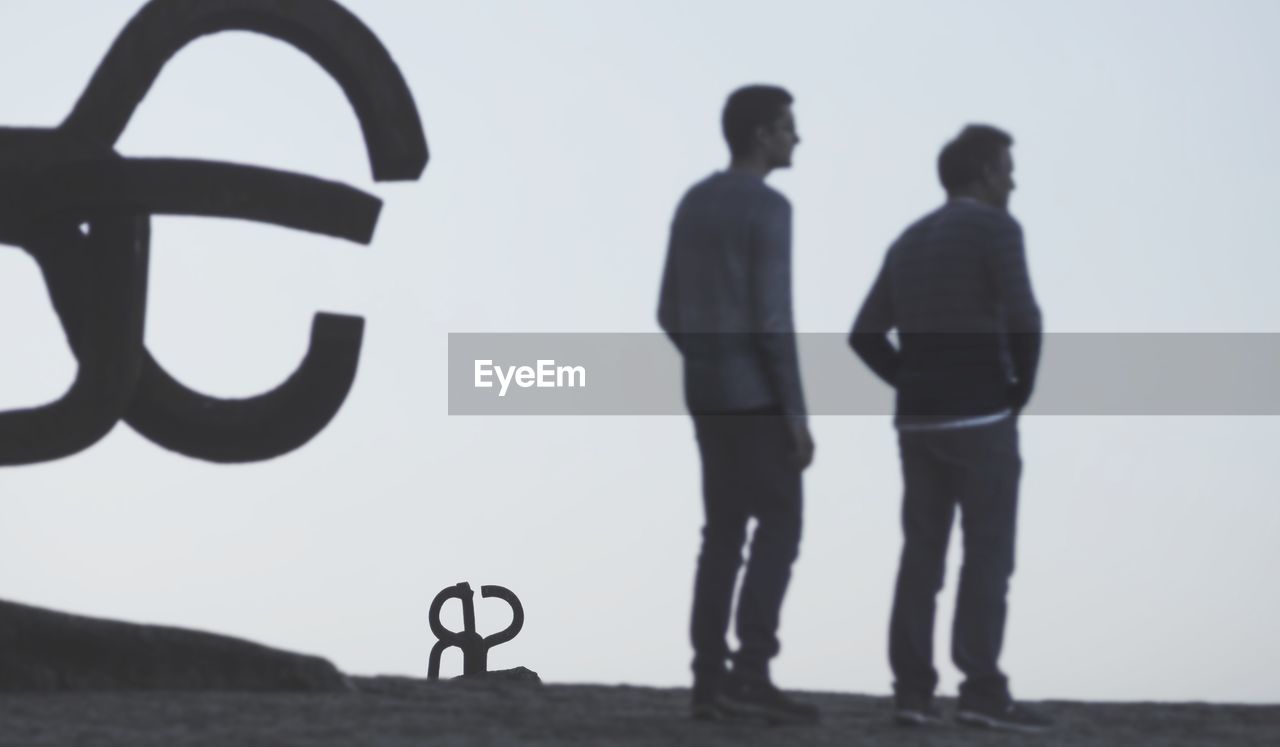 REAR VIEW OF SILHOUETTE MEN STANDING AGAINST SKY