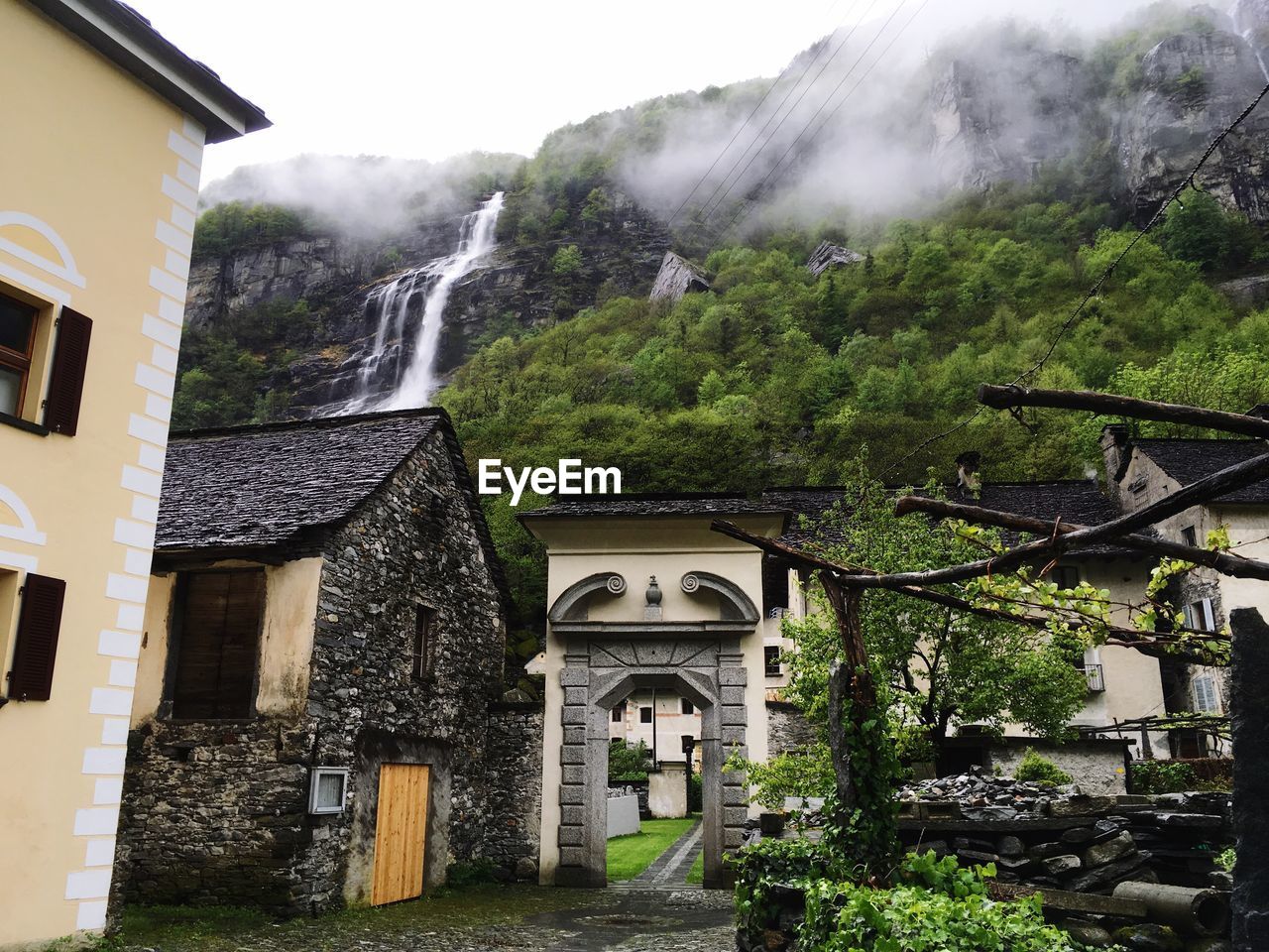 HOUSE AMIDST TREES AND BUILDINGS AGAINST MOUNTAINS