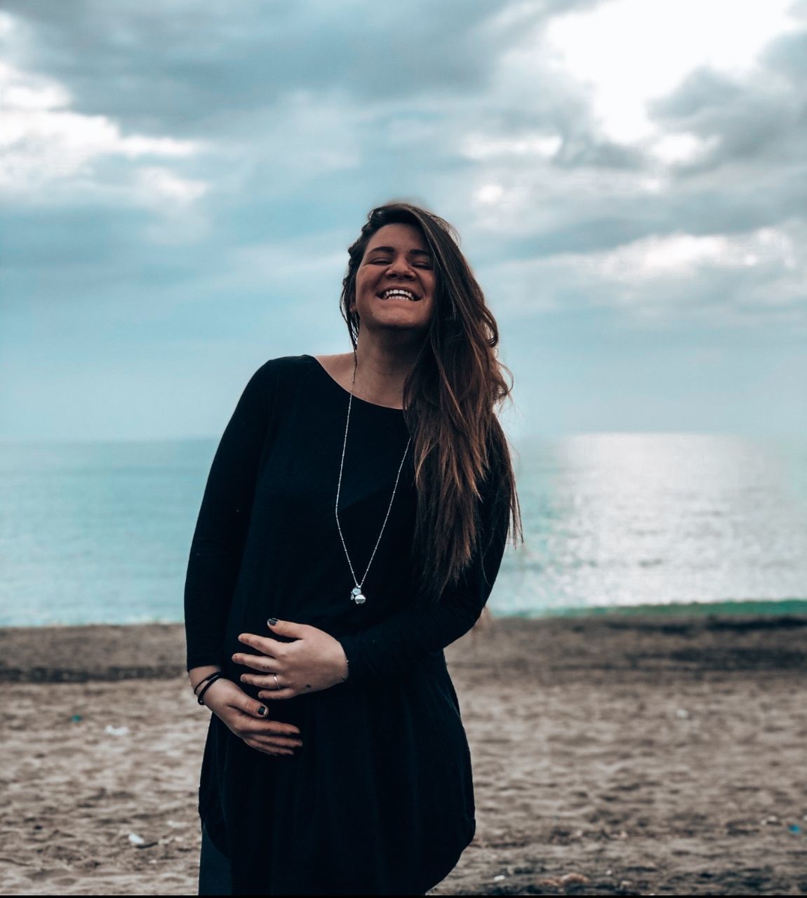 YOUNG WOMAN STANDING ON BEACH AGAINST SKY