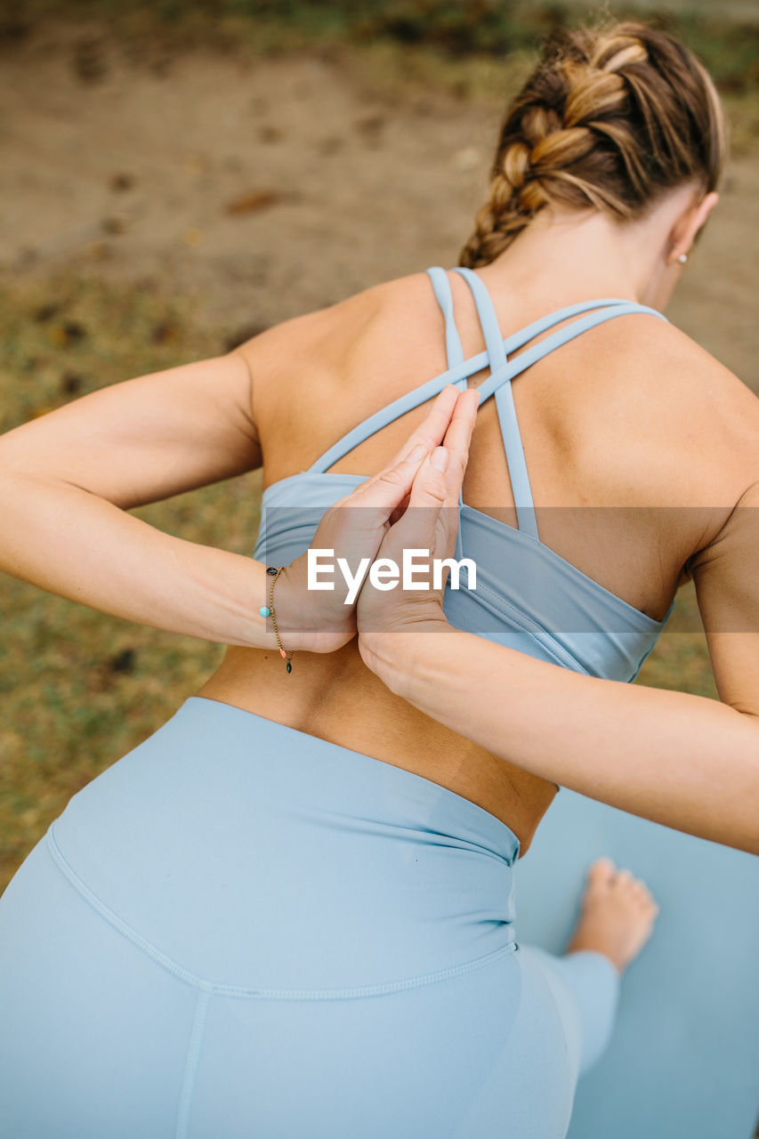 Back view of slim female in sportswear doing half pyramid pose with prayer hands behind back while practicing yoga in nature