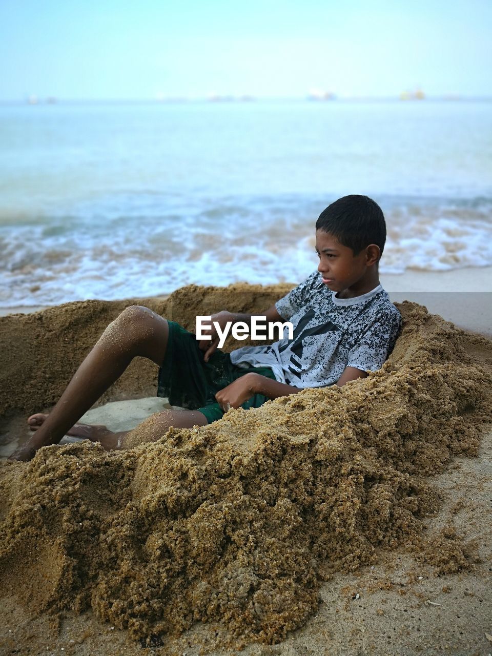 Boy sitting at beach against sky