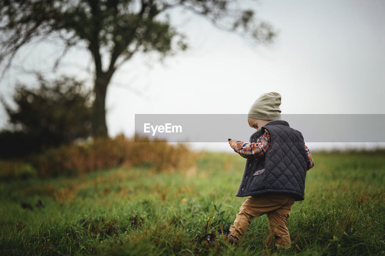 Rear view of boy standing on grassy field against sky