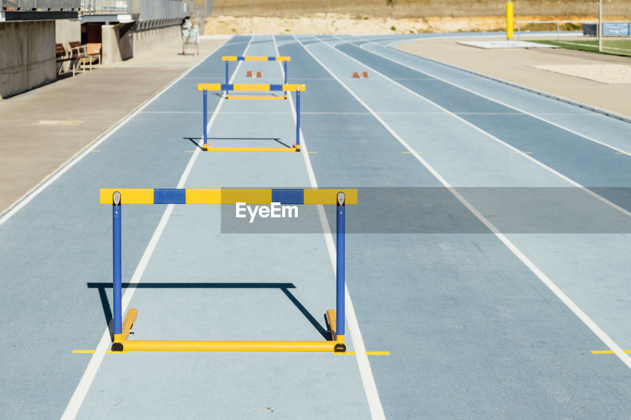 Row of colorful hurdles placed on blue racetrack during track and field workout on sunny day on stadium