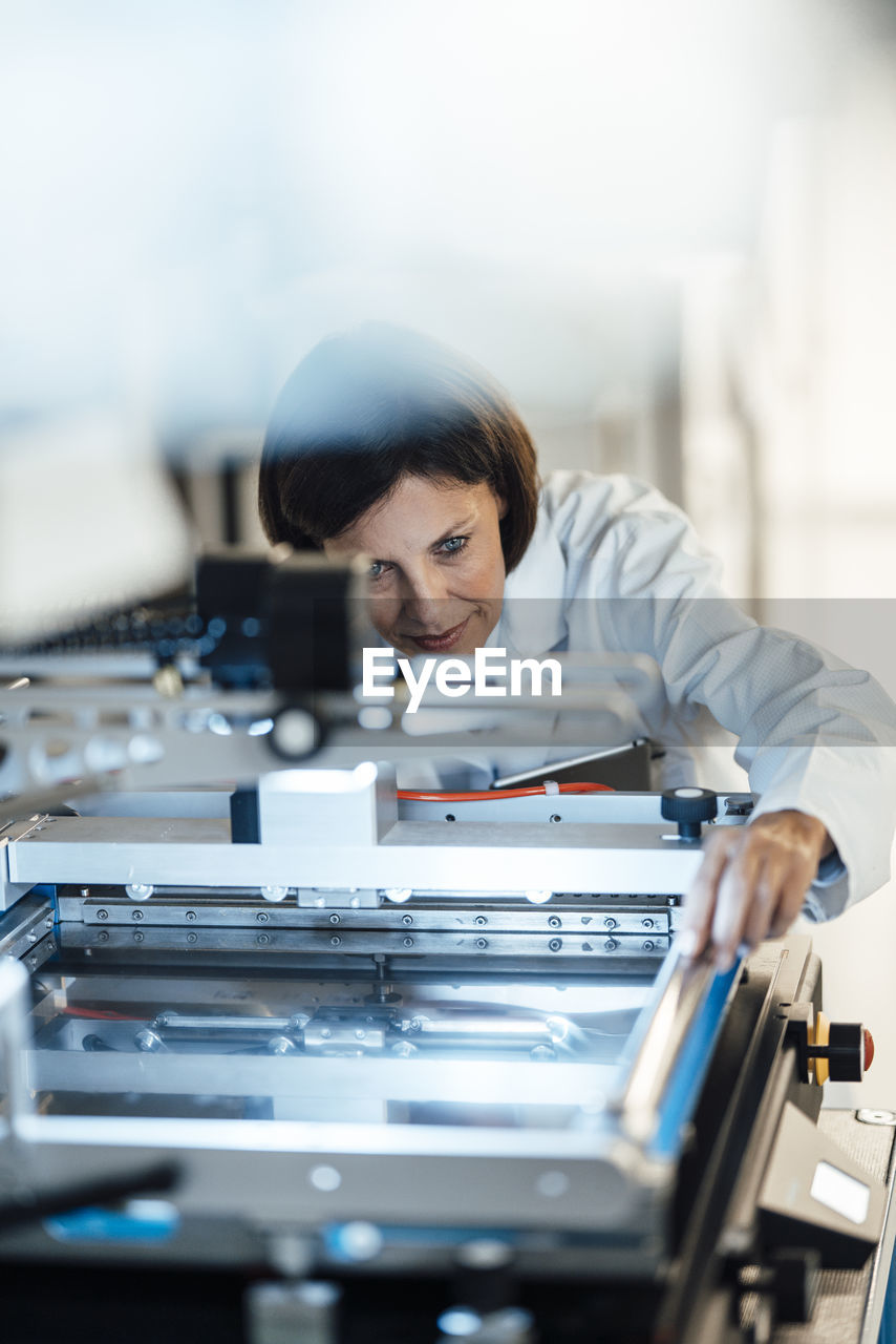 Mature businesswoman analyzing machinery in illuminated industry