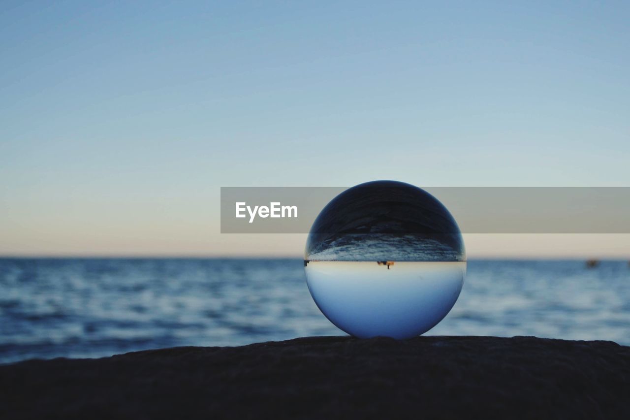 Light bulb on rock by sea against clear sky