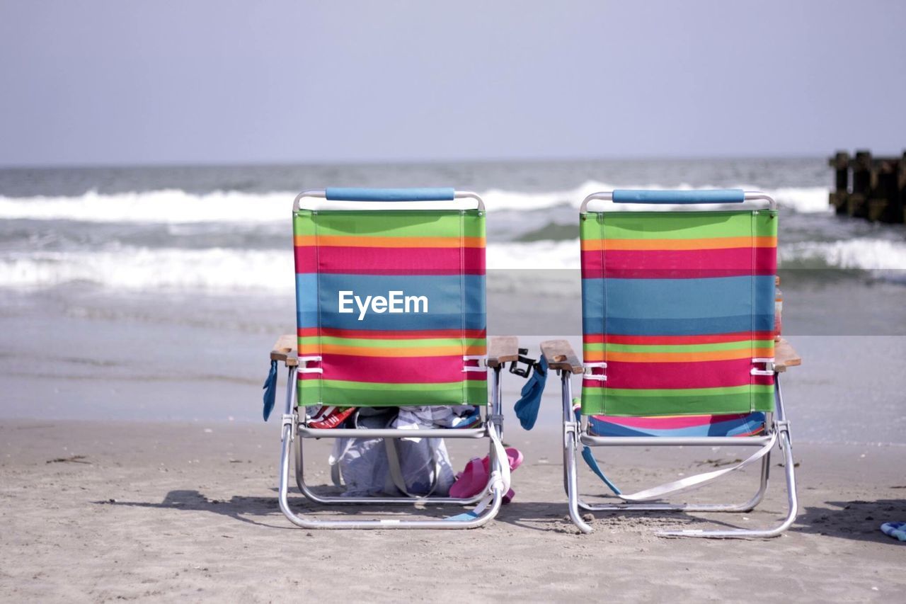 Colorful folding chairs on shore at beach against sky