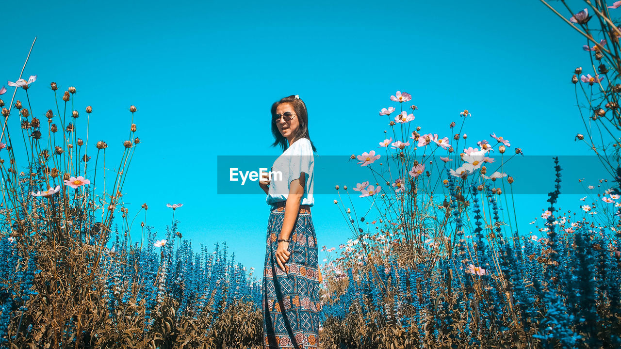 Young woman standing on field against sky