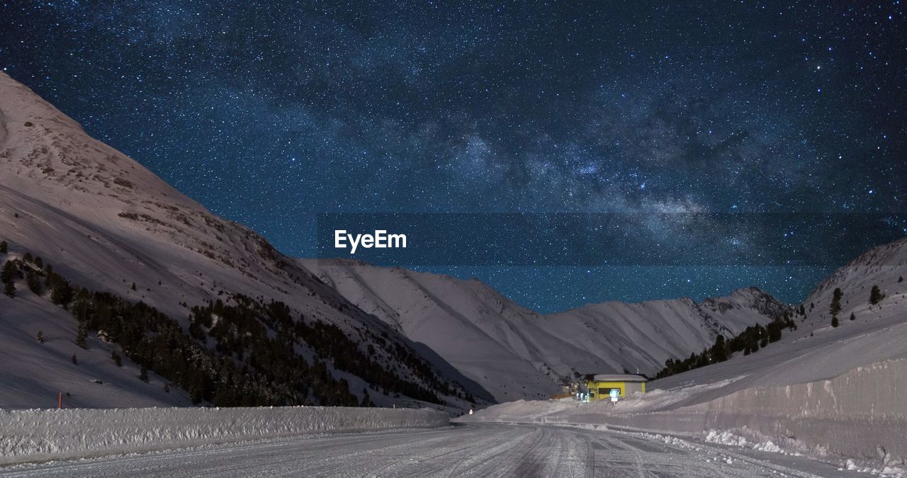 Road amidst snowcapped mountains against sky at night