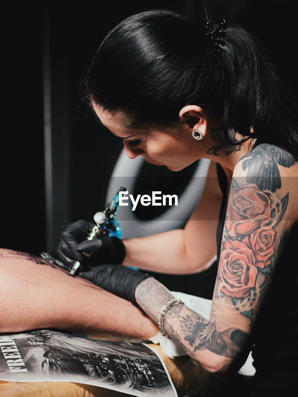 Young woman tattooing statue of liberty man on calf at parlor