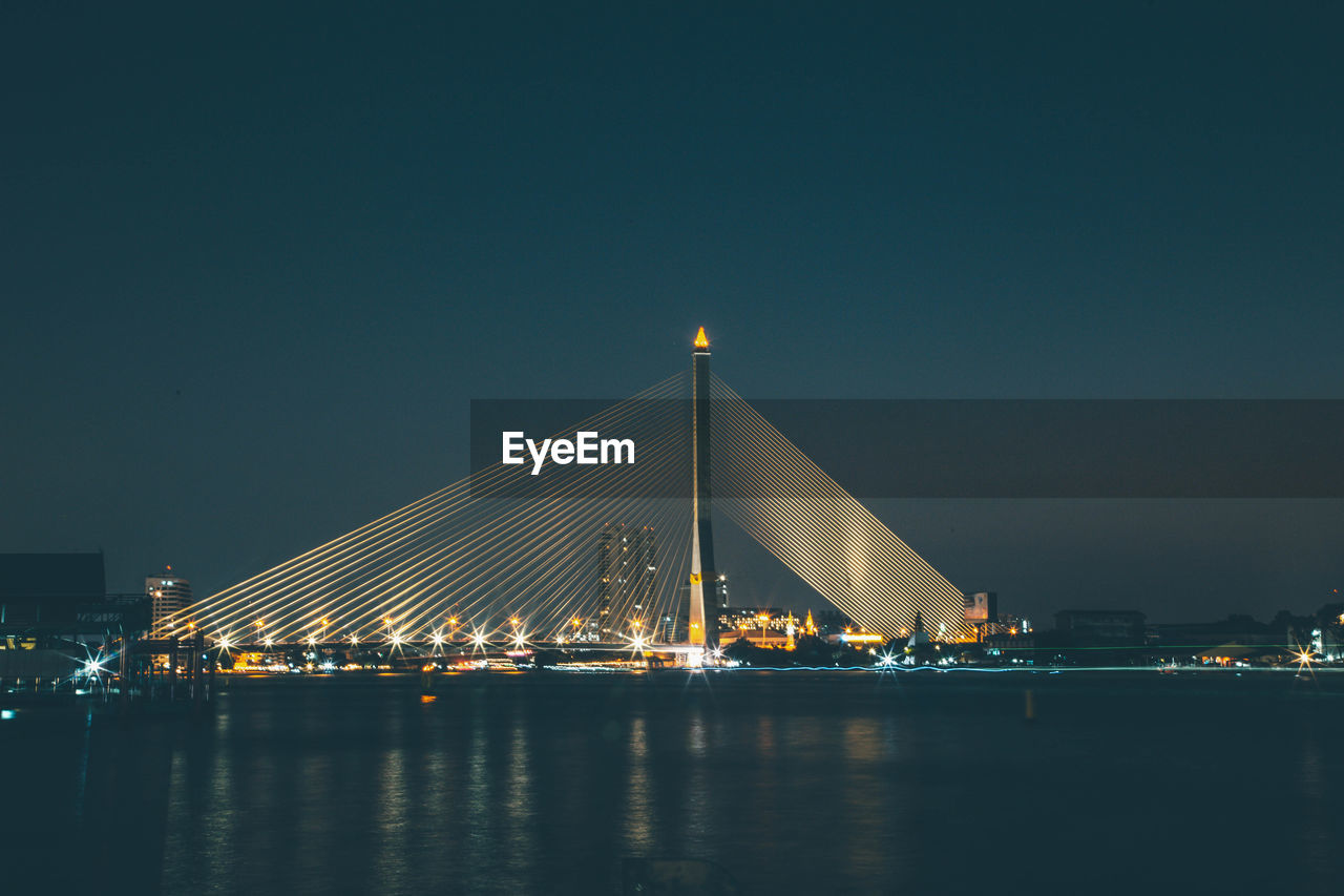 Illuminated bridge over river against sky at night