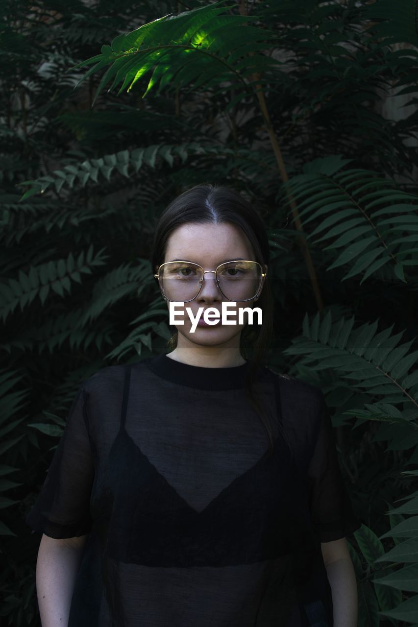 Portrait of young woman standing against plants