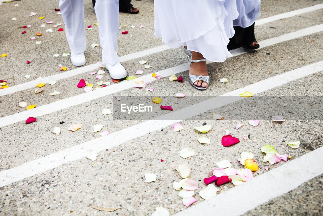 Low section of bride and groom walking on rose petals at street
