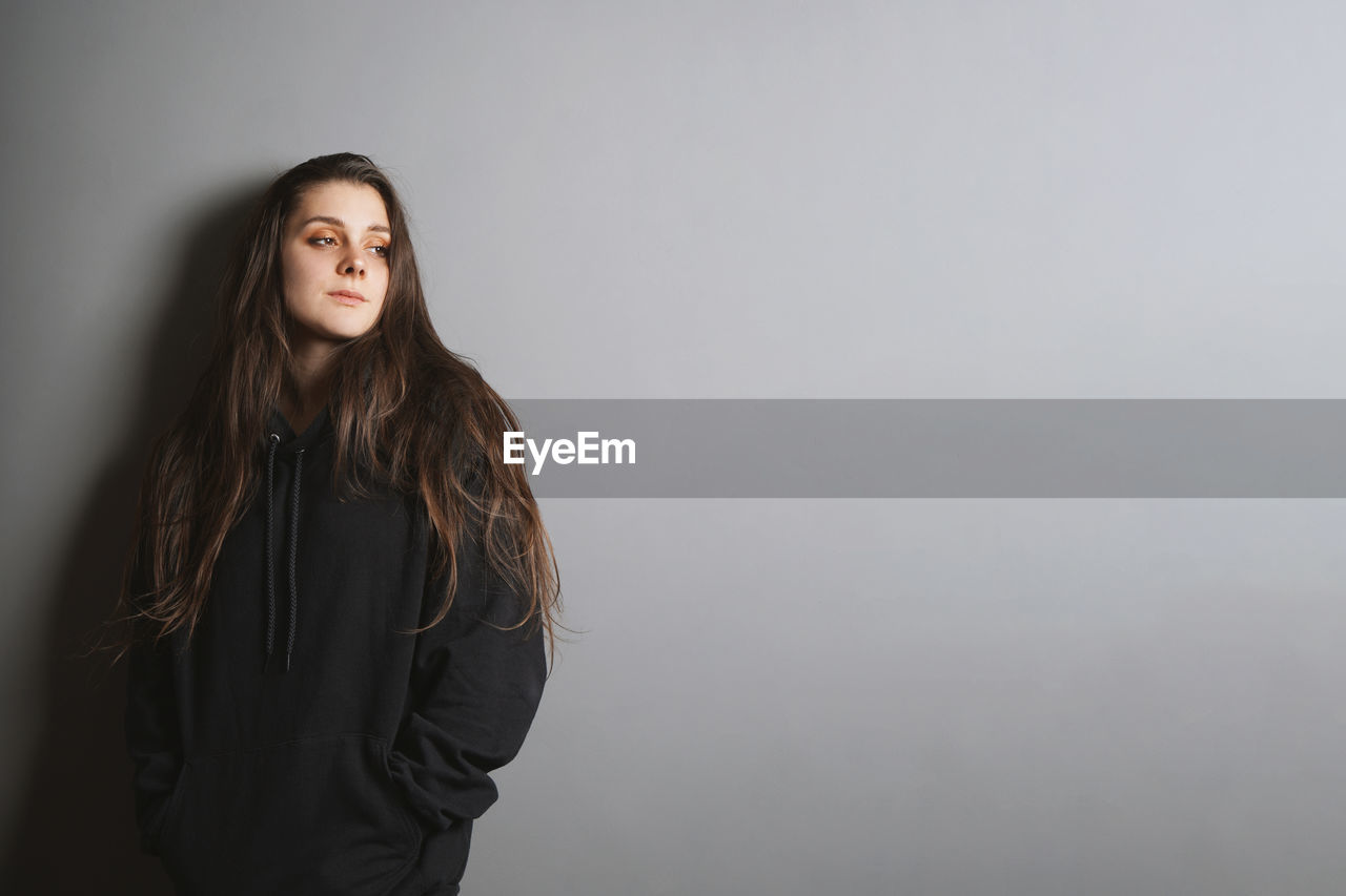 Young woman looking away while standing against gray background