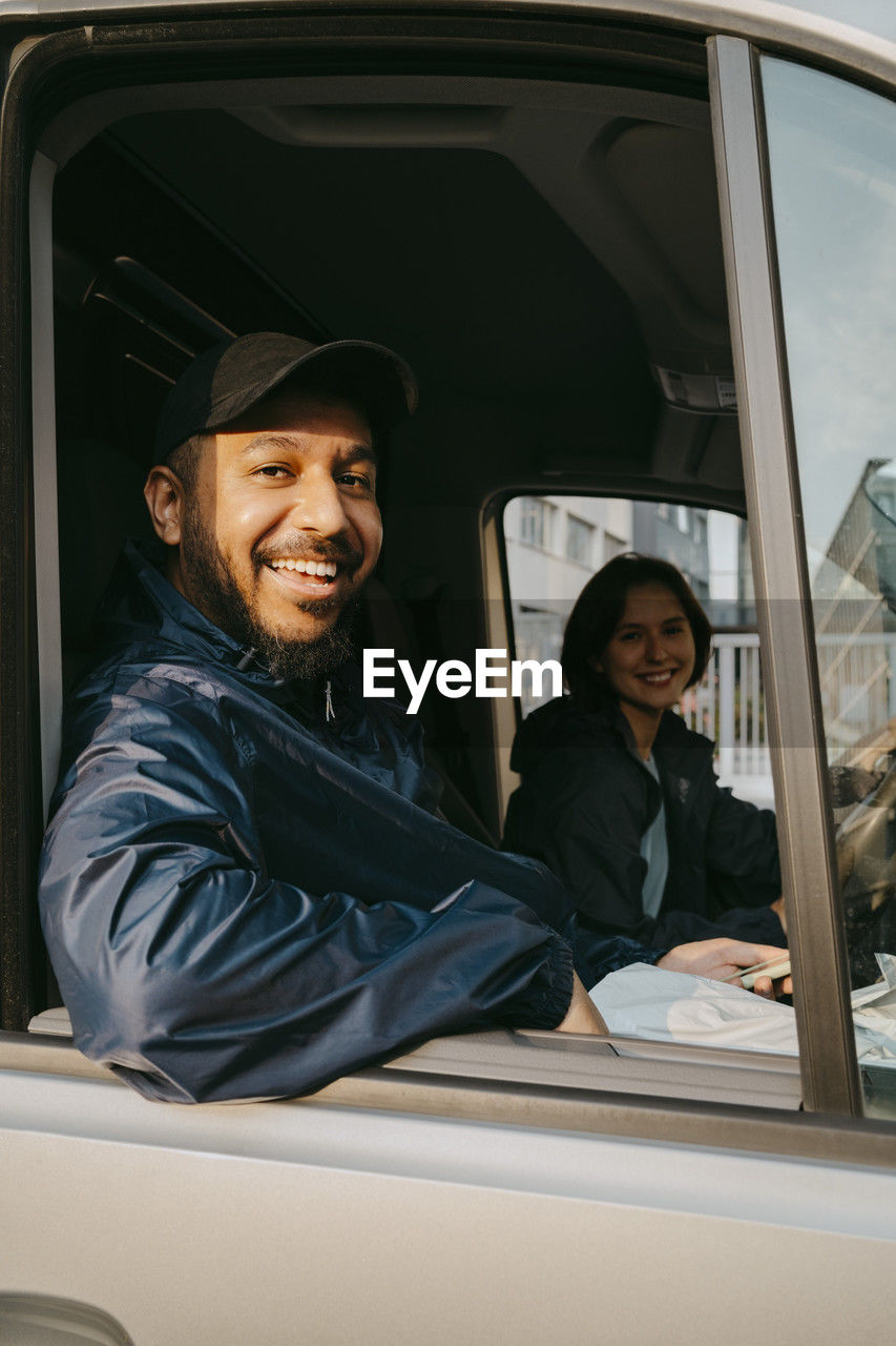 Portrait of smiling male delivery person sitting with female colleague in van