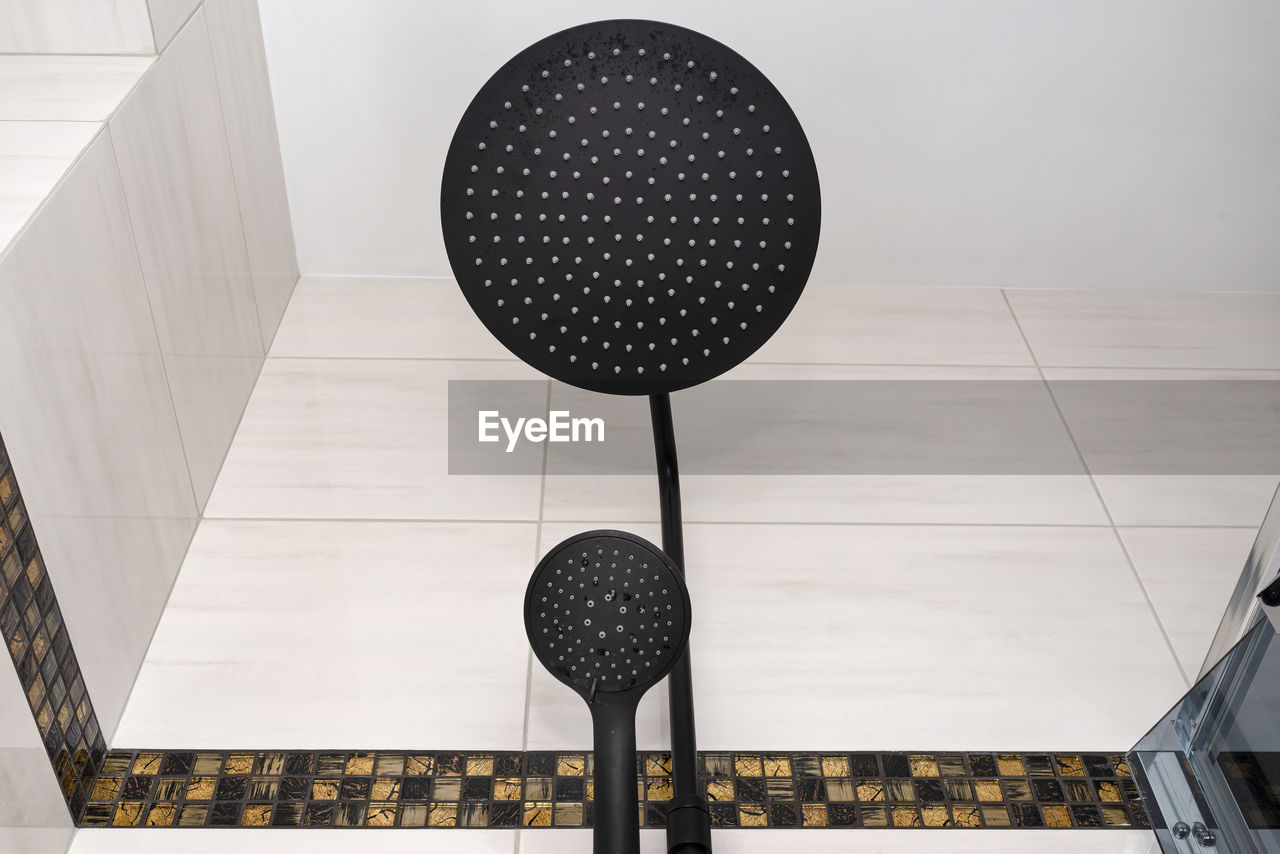 A modern, black metal shower with small and large rain shower, placed on tiles.