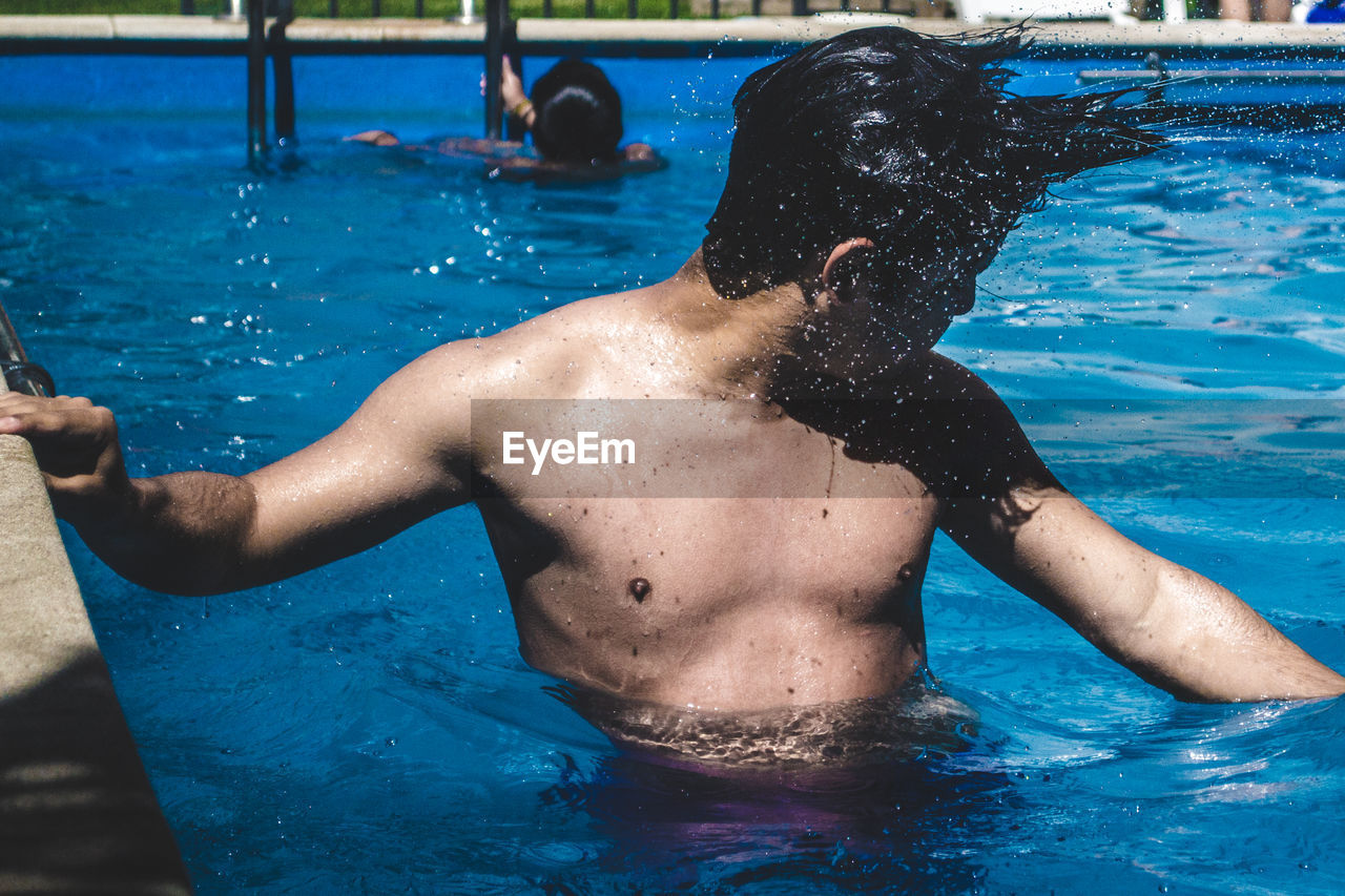 Shirtless young man splashing water in swimming pool