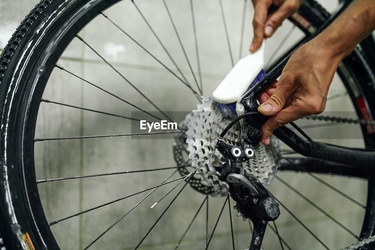 Unrecognizable crop male mechanic cleaning gear cassette of bicycle wheel with brush in workshop