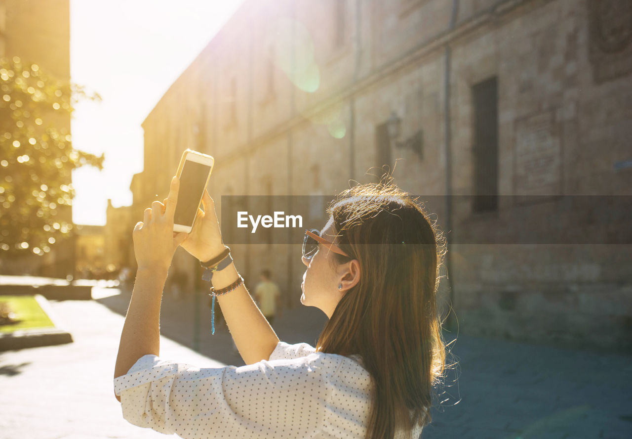 Young woman photographing through phone on street