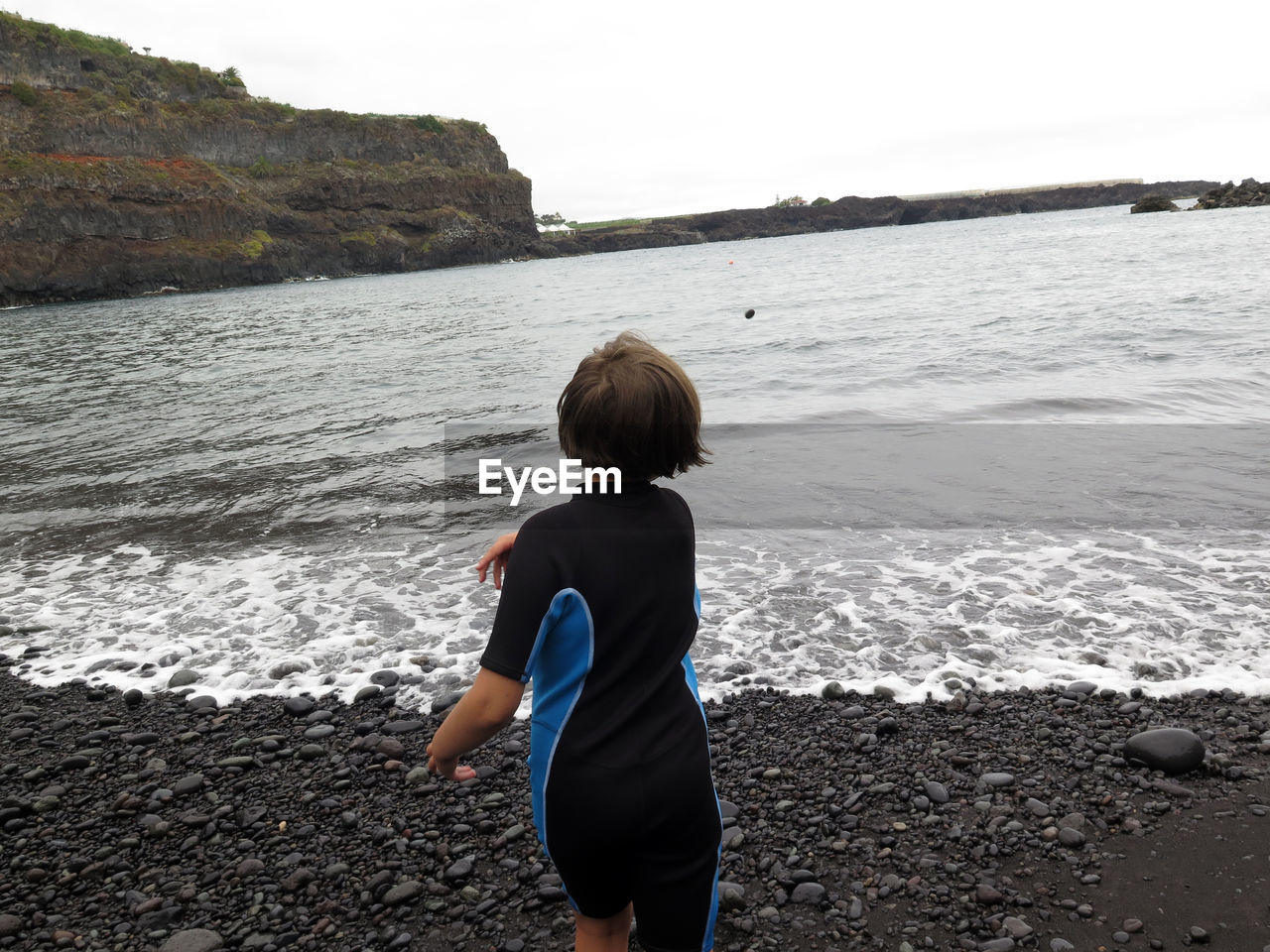 Rear view of girl throwing stones in sea