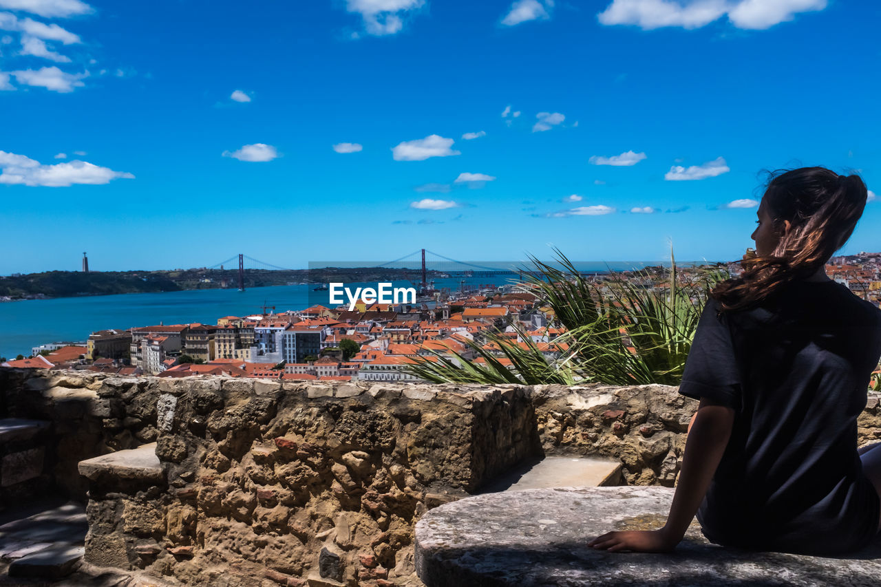 A teenager girl looking the urban landscape of lisbon. the 25th of april bridge in the background. 