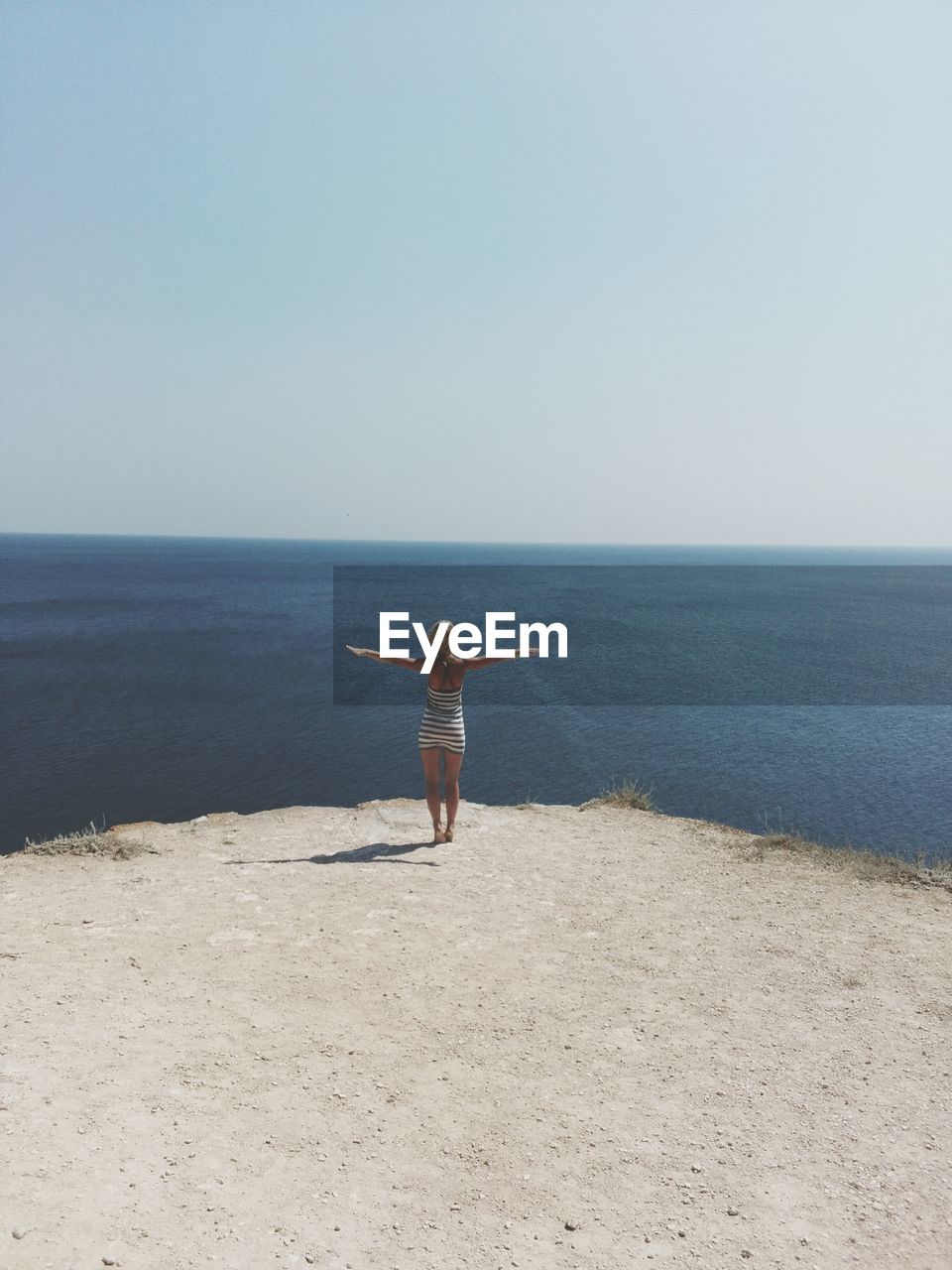 Rear view of woman with arms outstretched standing at beach against clear sky