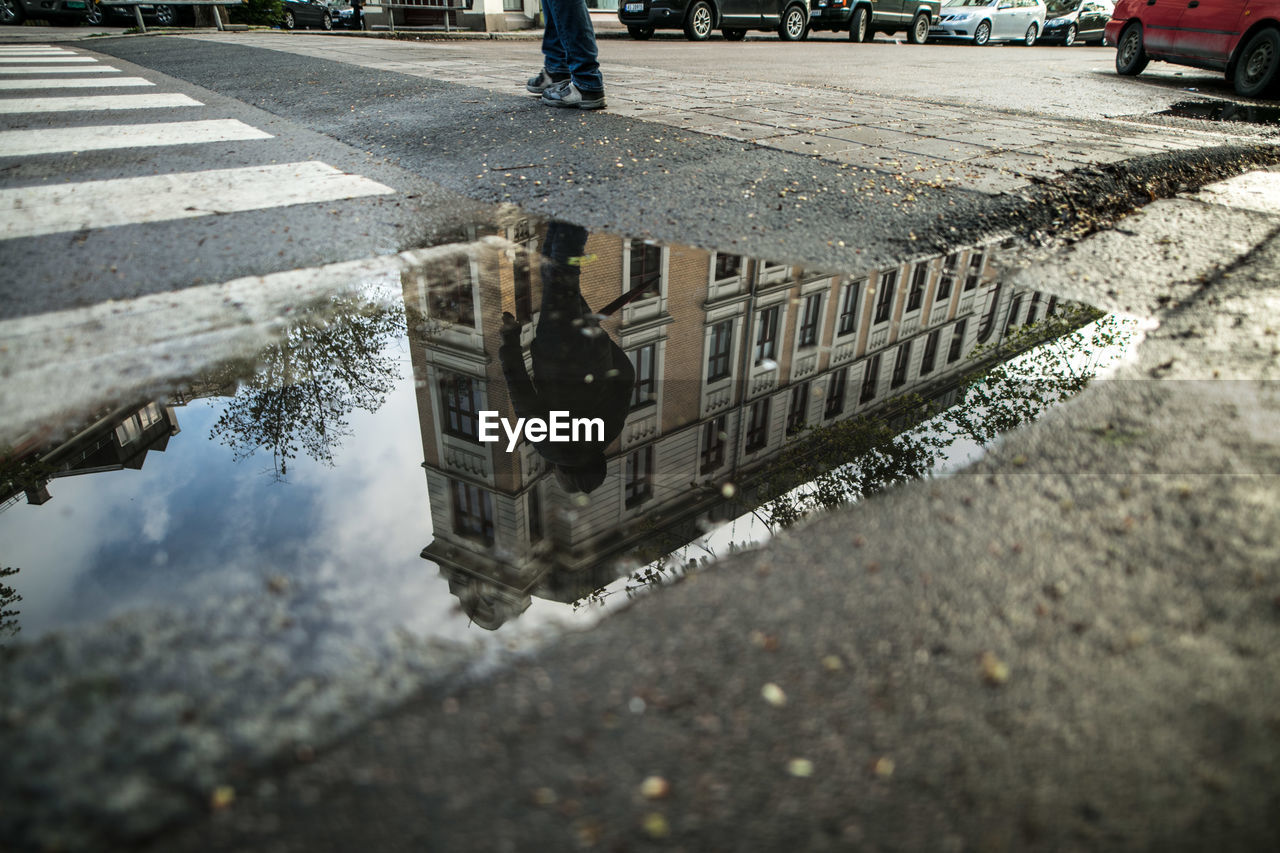 Reflection of man in puddle by zebra crossing while walking on road