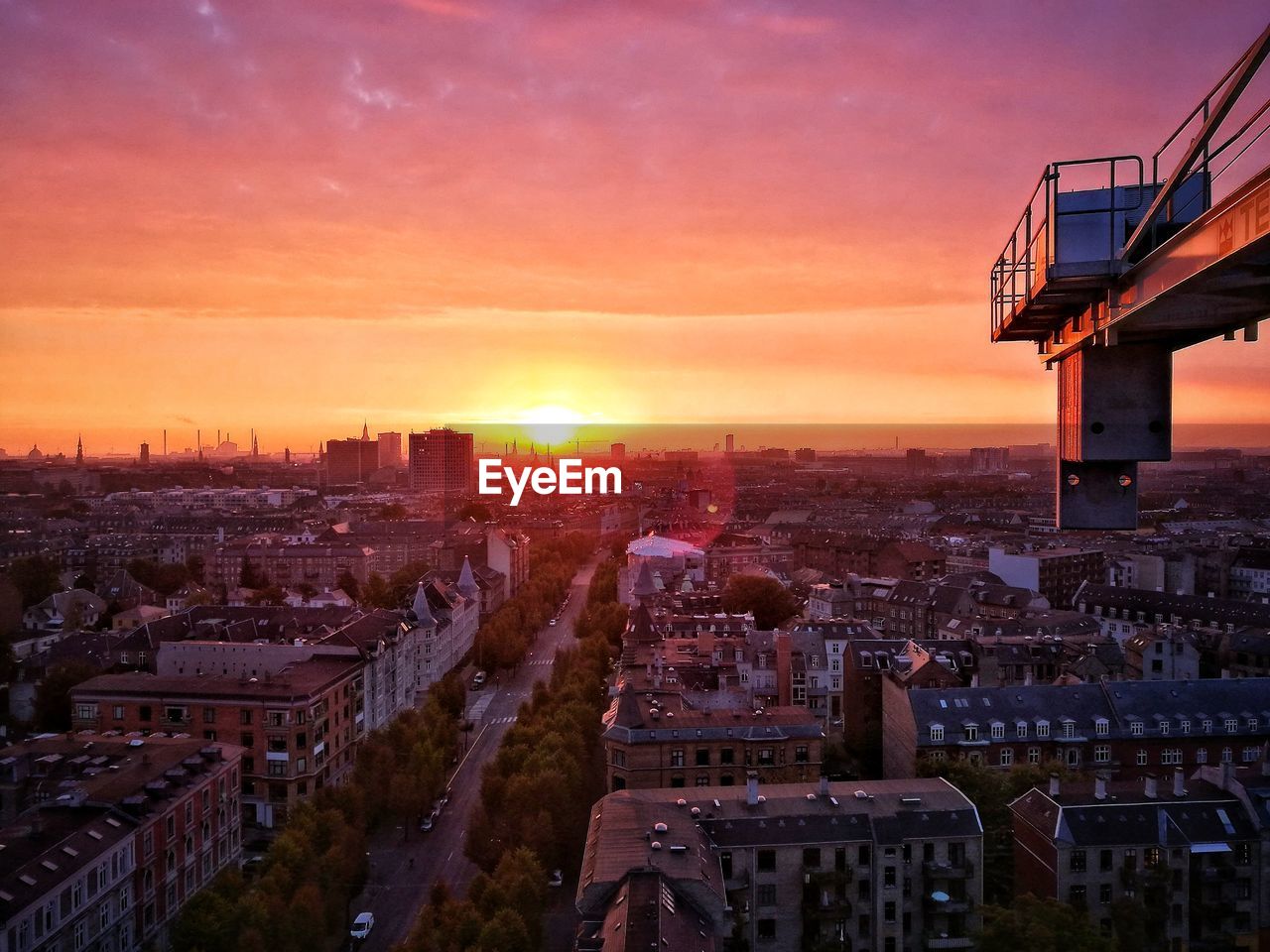 Cherry picker over cityscape against sky during sunset