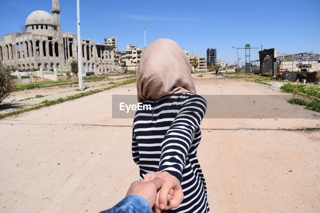 Cropped image of man holding woman hand standing on road