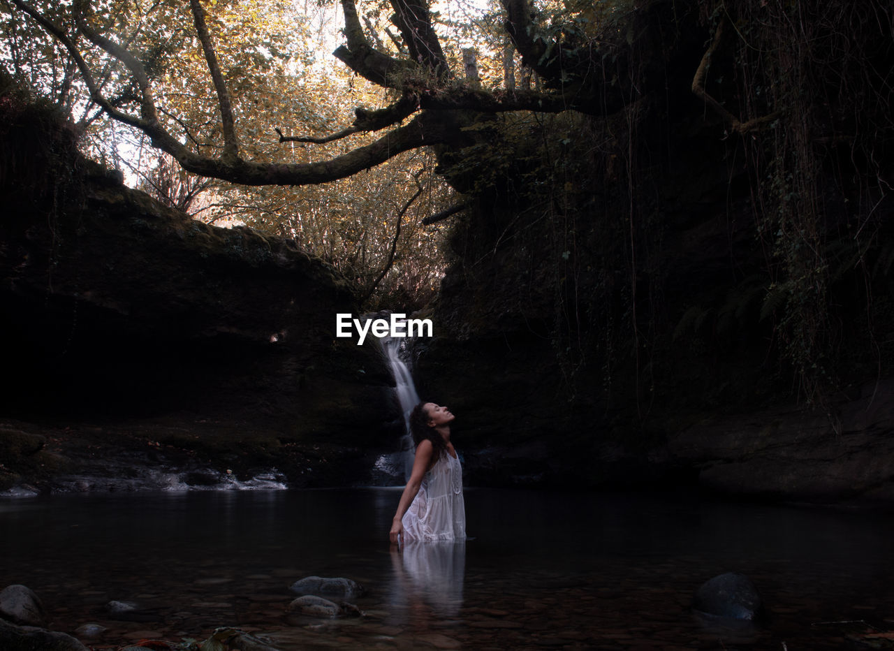 WOMAN STANDING ON ROCK IN WATER AT FOREST
