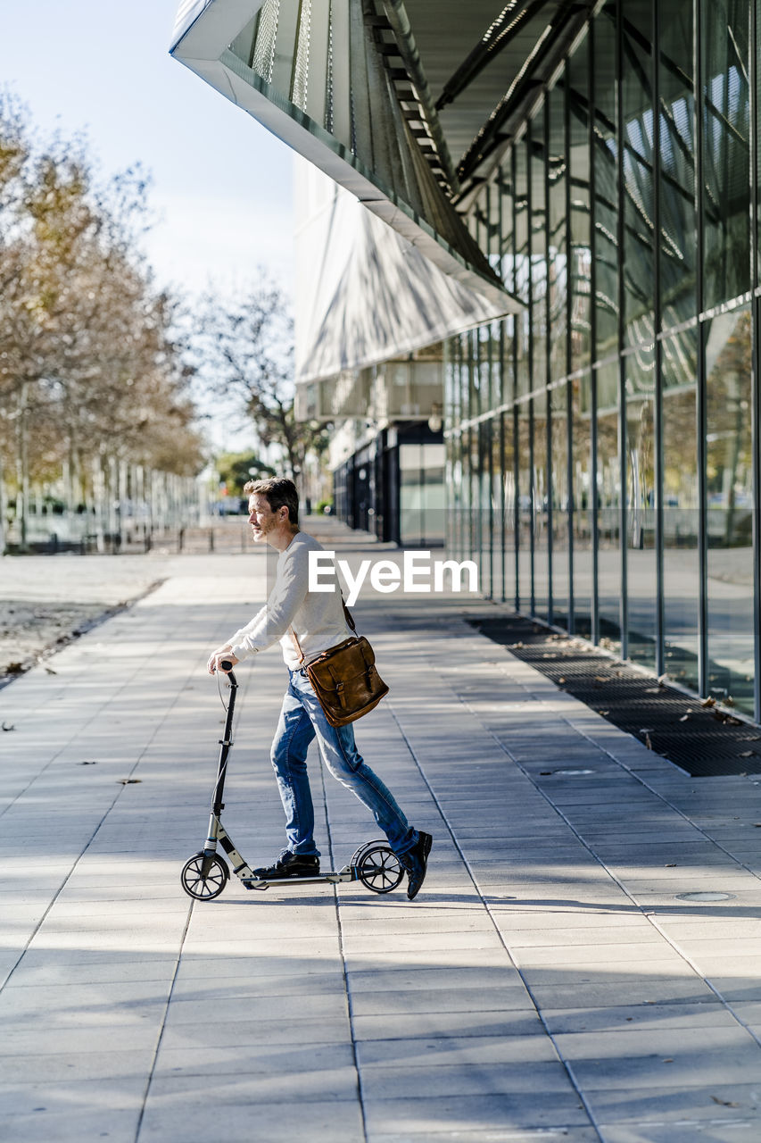 Mature man commuting in the city, using kick scooter on the pavement