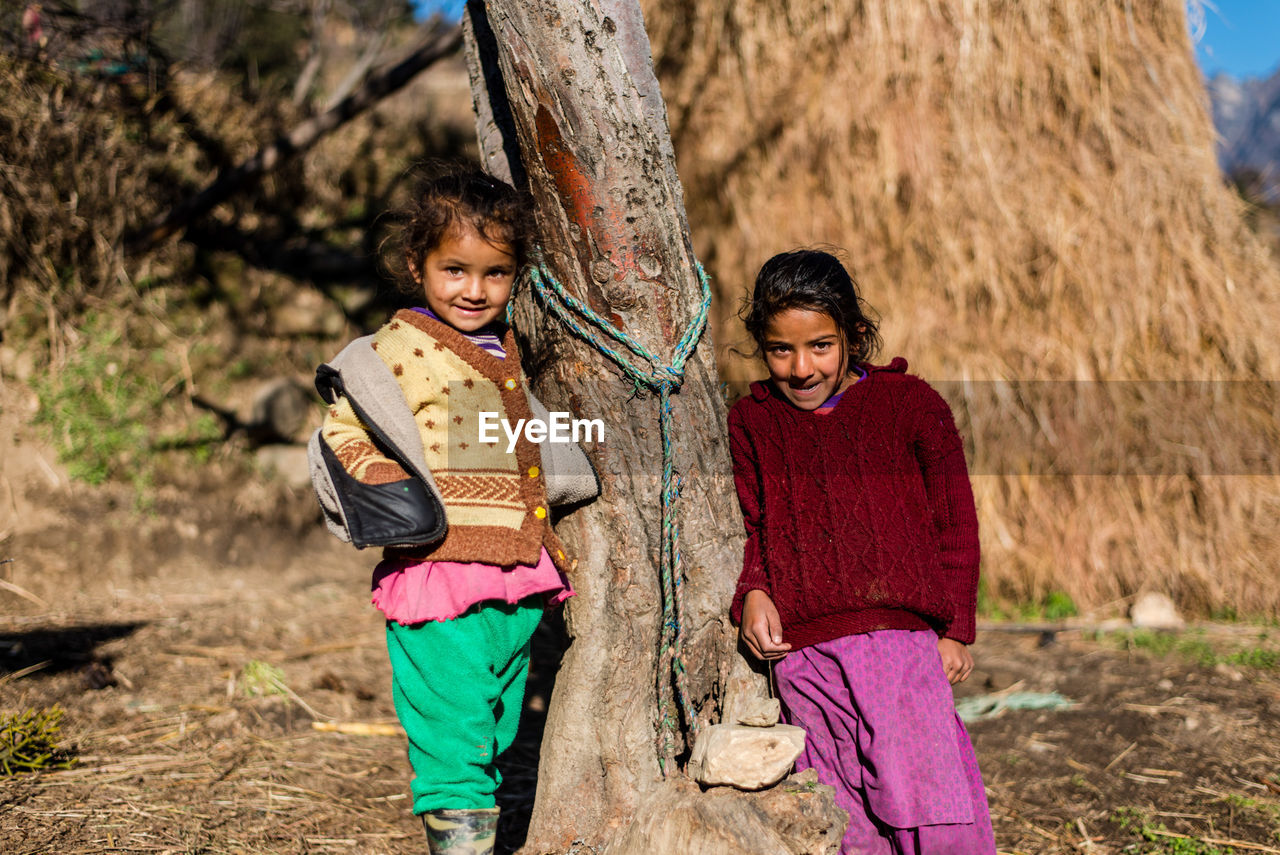 PORTRAIT OF A SMILING GIRL STANDING AGAINST TREE