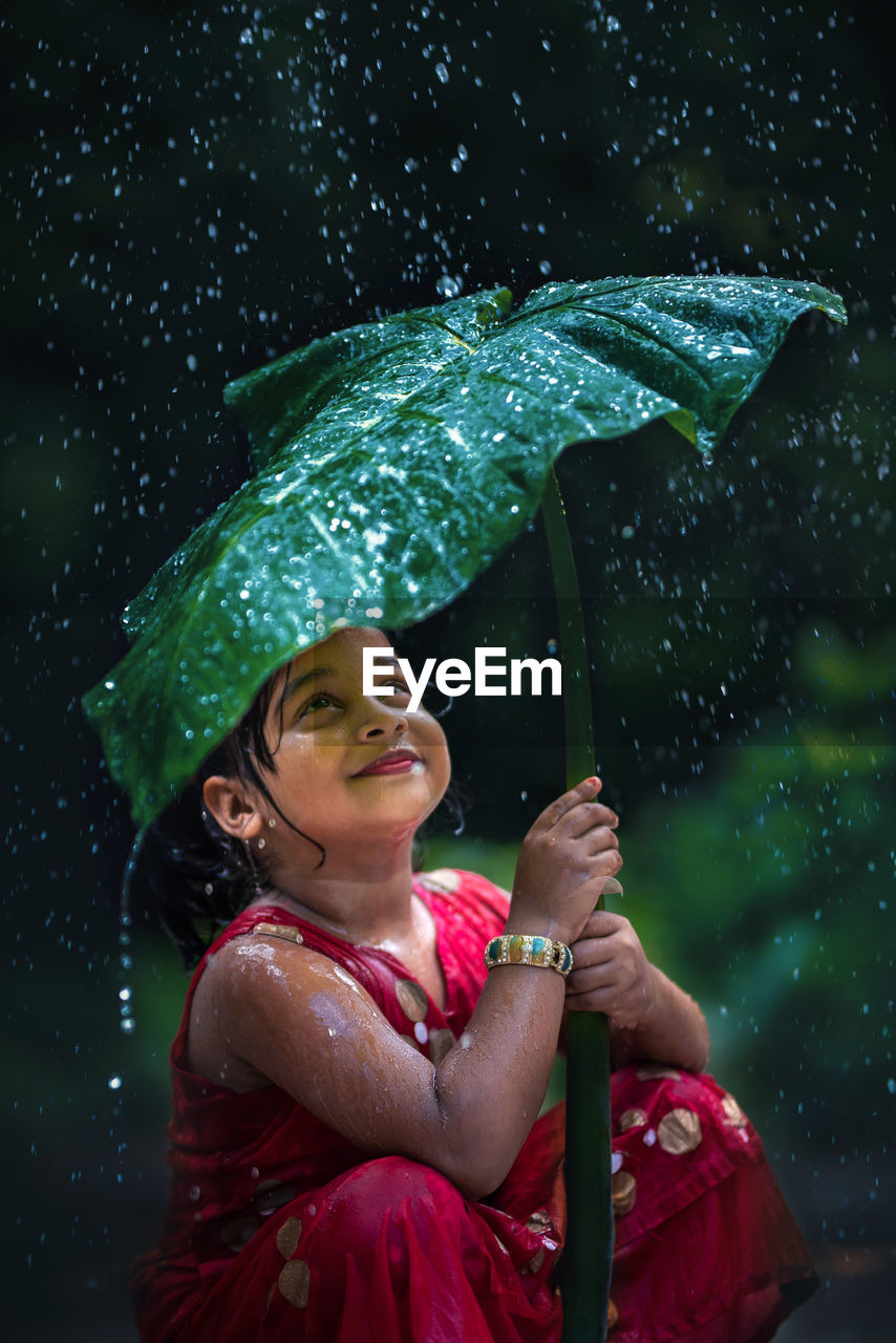 Portrait of smiling girl holding umbrella during rainy season