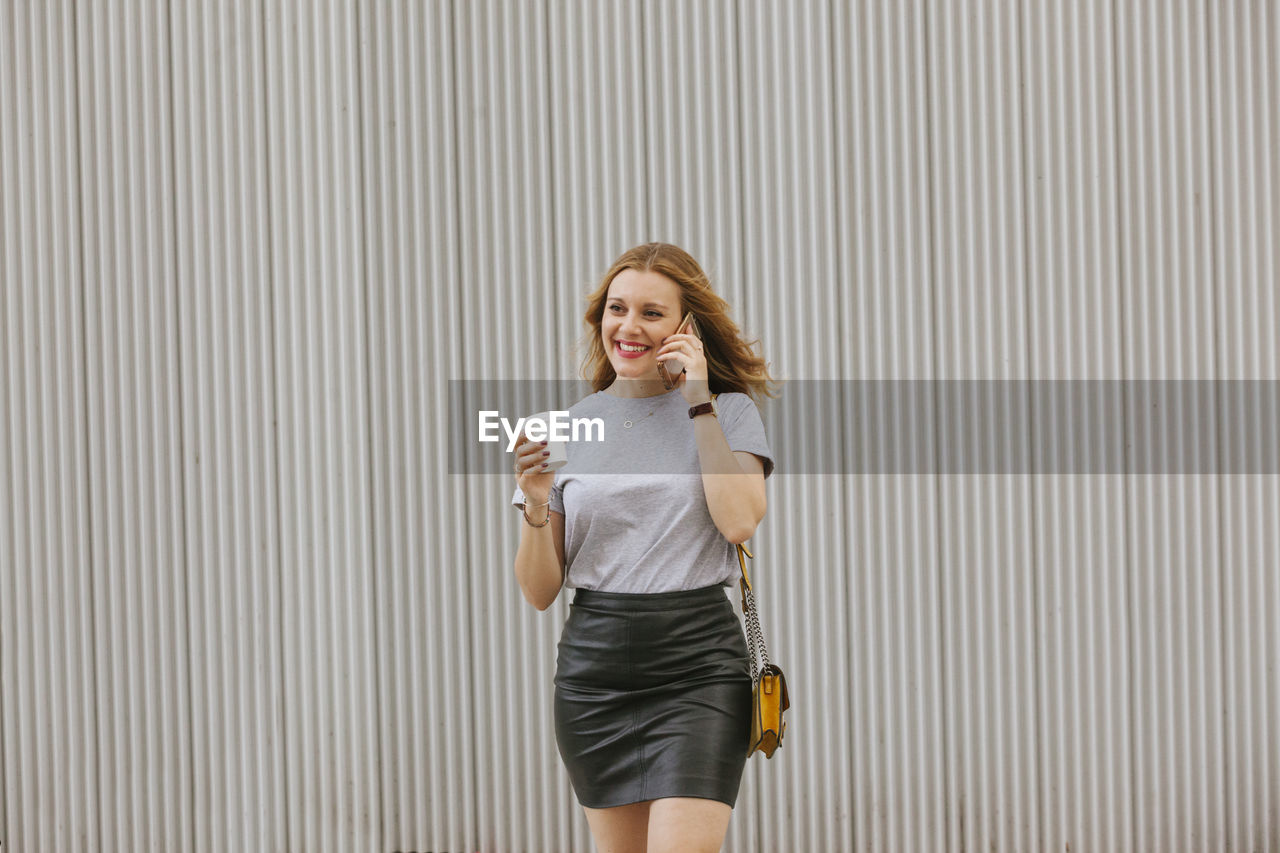 Smiling woman talking on phone while walking in city