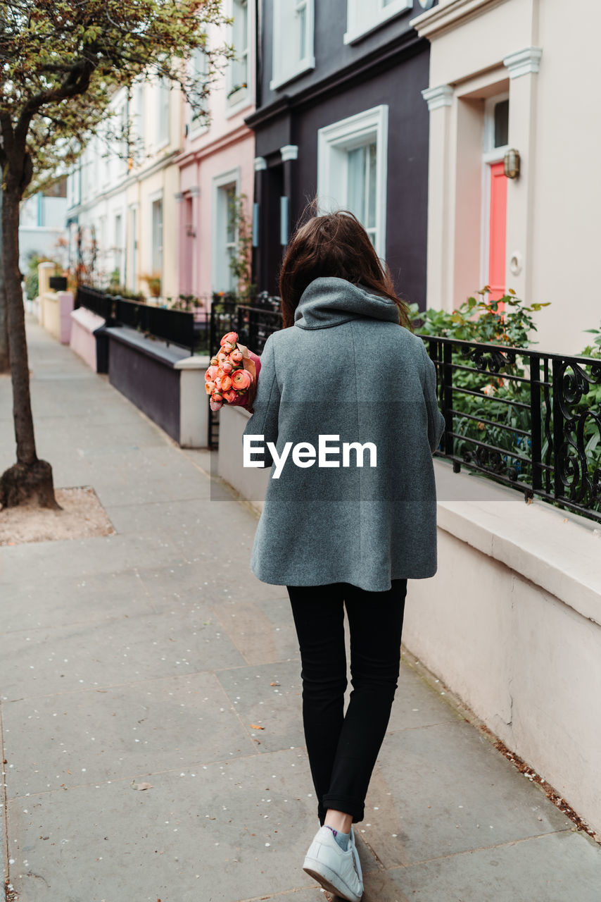 Rear view of woman standing on footpath by street