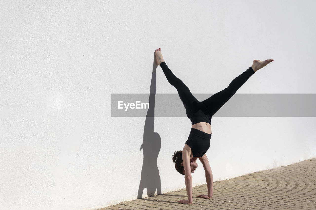 Woman doing a handstand against a white wall in the sun
