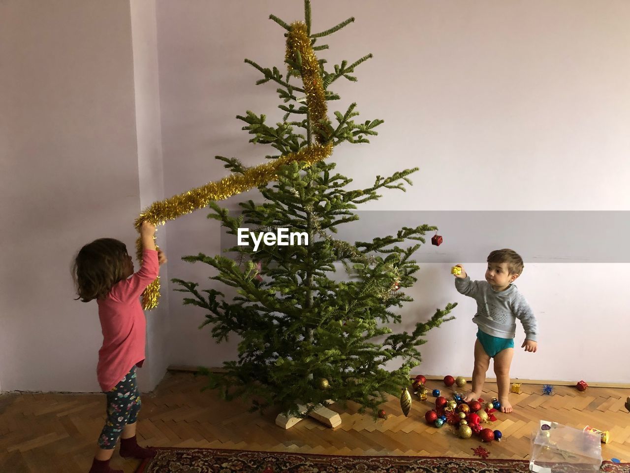 Siblings playing with christmas tree at home
