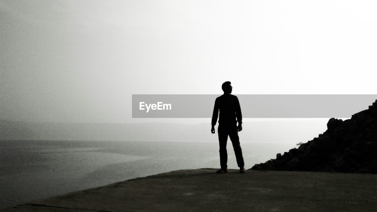Rear view of a silhouette man overlooking calm sea