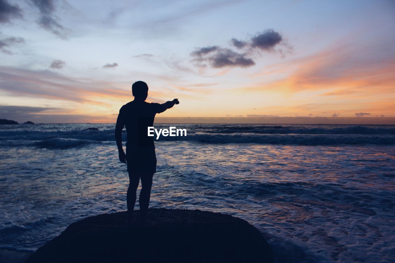 Silhouette man standing on rock at beach during sunset