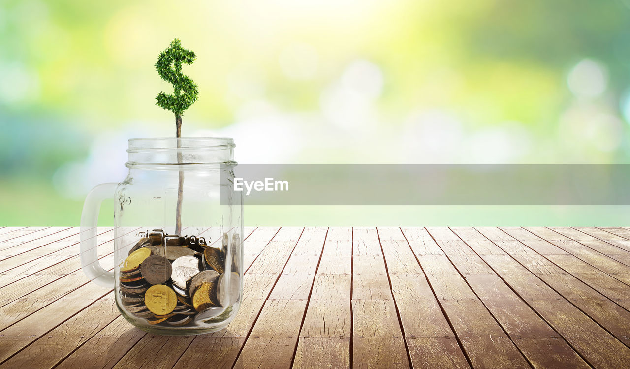 Close-up of dollar symbol and coins in mason jar on wooden table