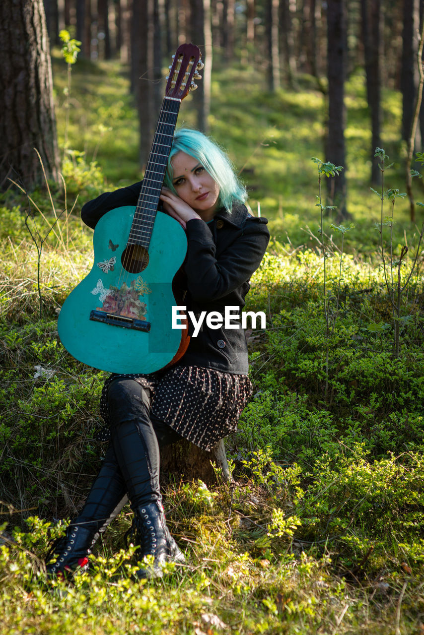 Hipster young woman with turquoise guitar sitting in forest