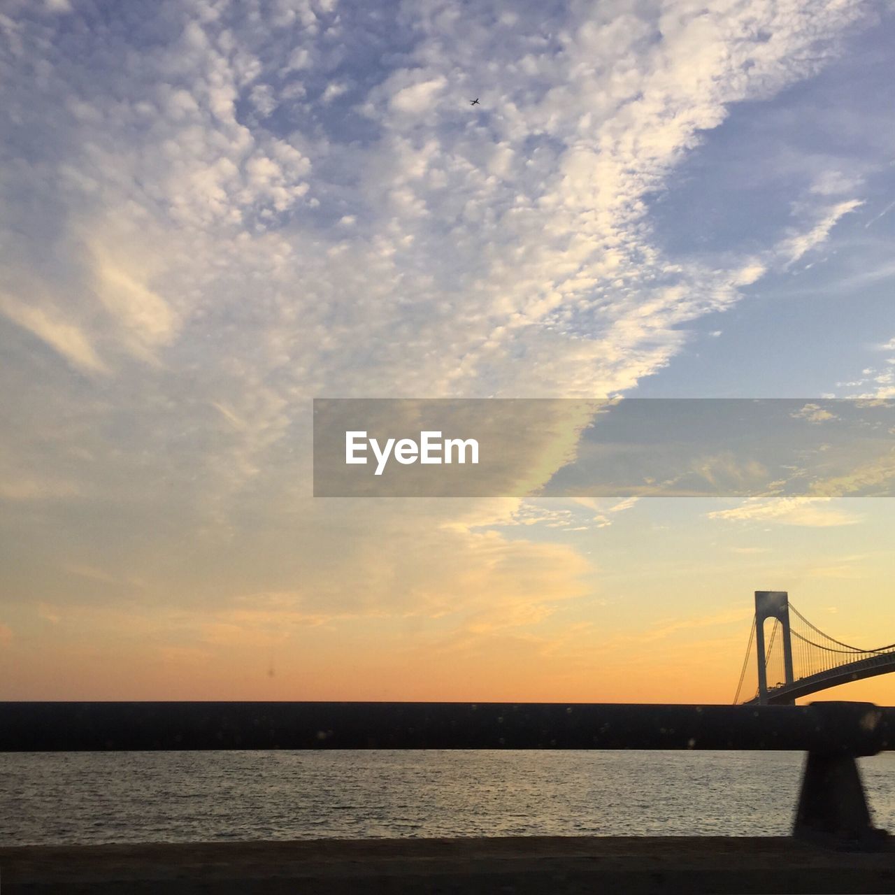 Verrazano-narrows bridge over river against cloudy sky during sunset